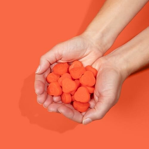 Hands holding small orange heart-shaped objects on an orange background.