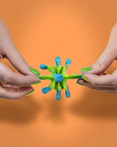 Hands holding a colorful sticky toy against an orange background.