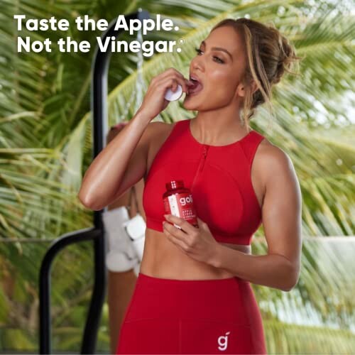 Woman in red activewear eating a gummy supplement with a bottle in hand.